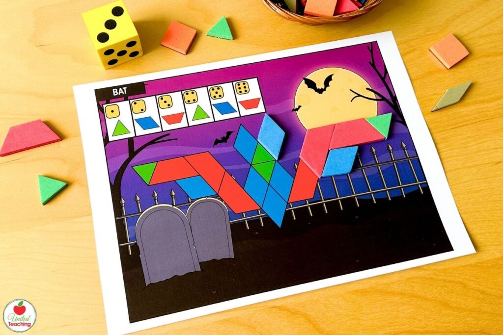 Roll and build Halloween bat pattern block mat with a spooky cemetery and full moon scene, where students roll a die and place the matching shape to build the bat