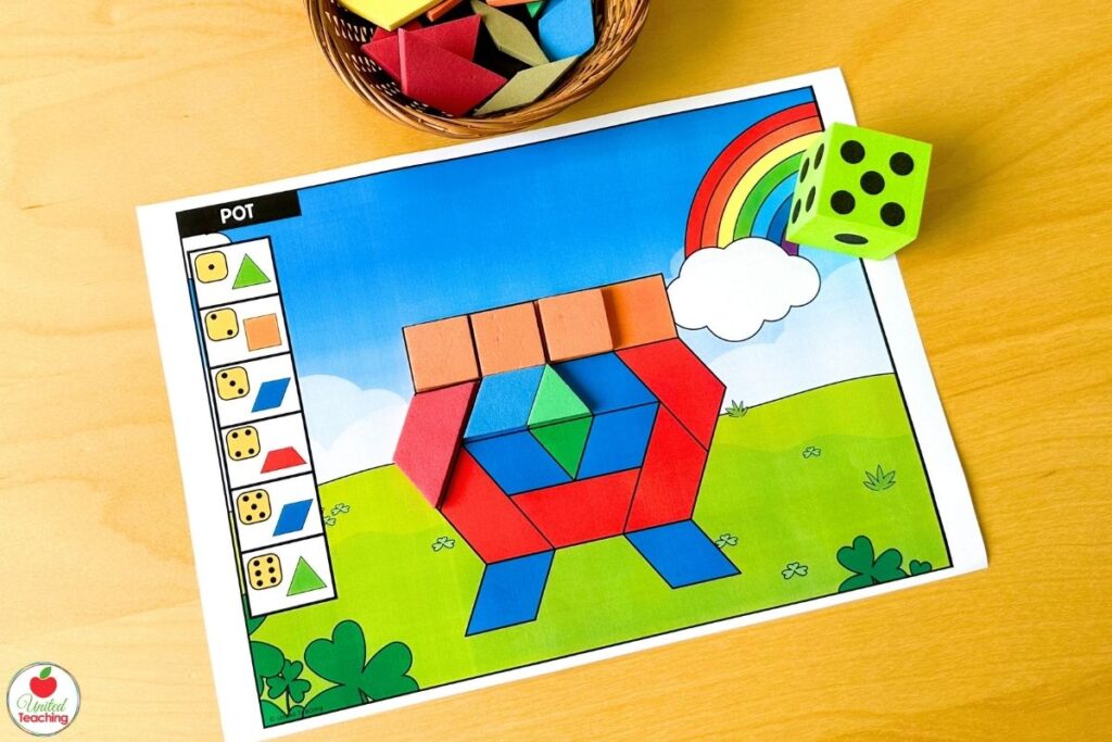 Roll and build St. Patrick's Day pot of gold pattern block mat with a rainbow and shamrock scene, where students roll a die and place the matching shape to build the pot