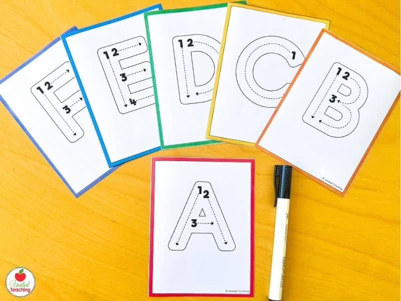 Uppercase letter formation task cards A through F fanned on a table with a dry-erase marker for reusable alphabet tracing practice