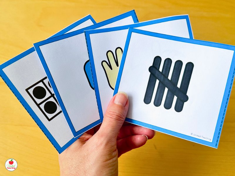 Hand holding subitizing flash cards showing different number representations including a domino, finger pattern, and tally marks